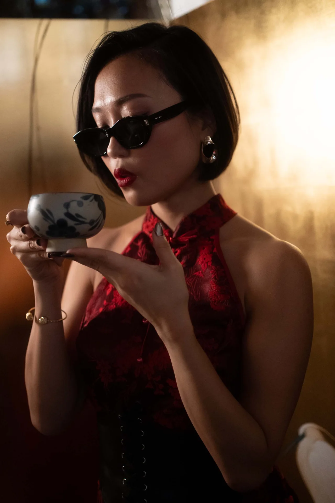 Crystal Chow in a red qipao, sipping tea in golden light
