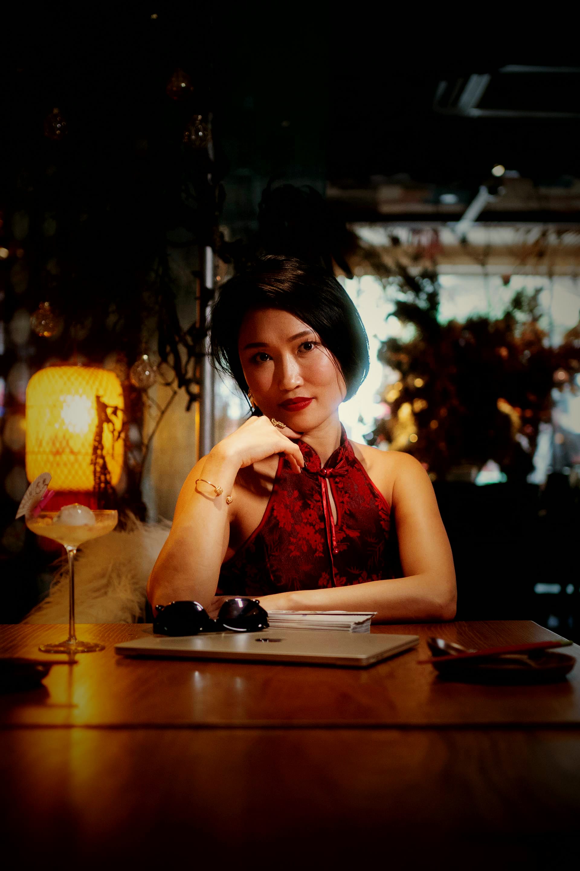 Crystal at a dark bar table, chin on hand, thinking